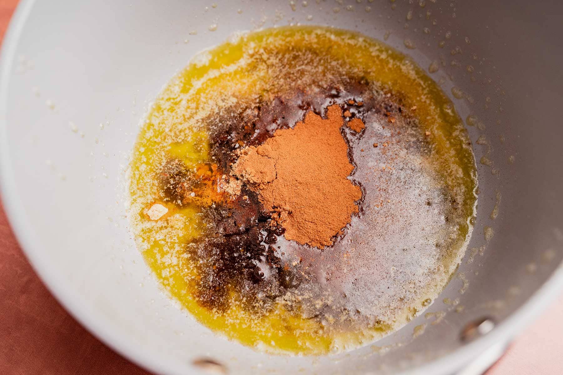 Melted butter, brown sugar, vanilla extract, and ground cinnamon are combined in a mixing bowl to create the perfect base for a festive Christmas snack mix.