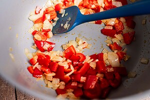 Chopped red bell peppers and onions being sautéed in a pan with a blue spatula—the perfect base for a hearty butter bean stew.