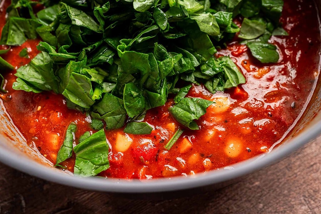 Close-up of a bowl of tomato-based butter bean stew with beans, topped with freshly chopped spinach.