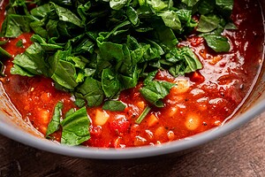 Close-up of a bowl of tomato-based butter bean stew with beans, topped with freshly chopped spinach.