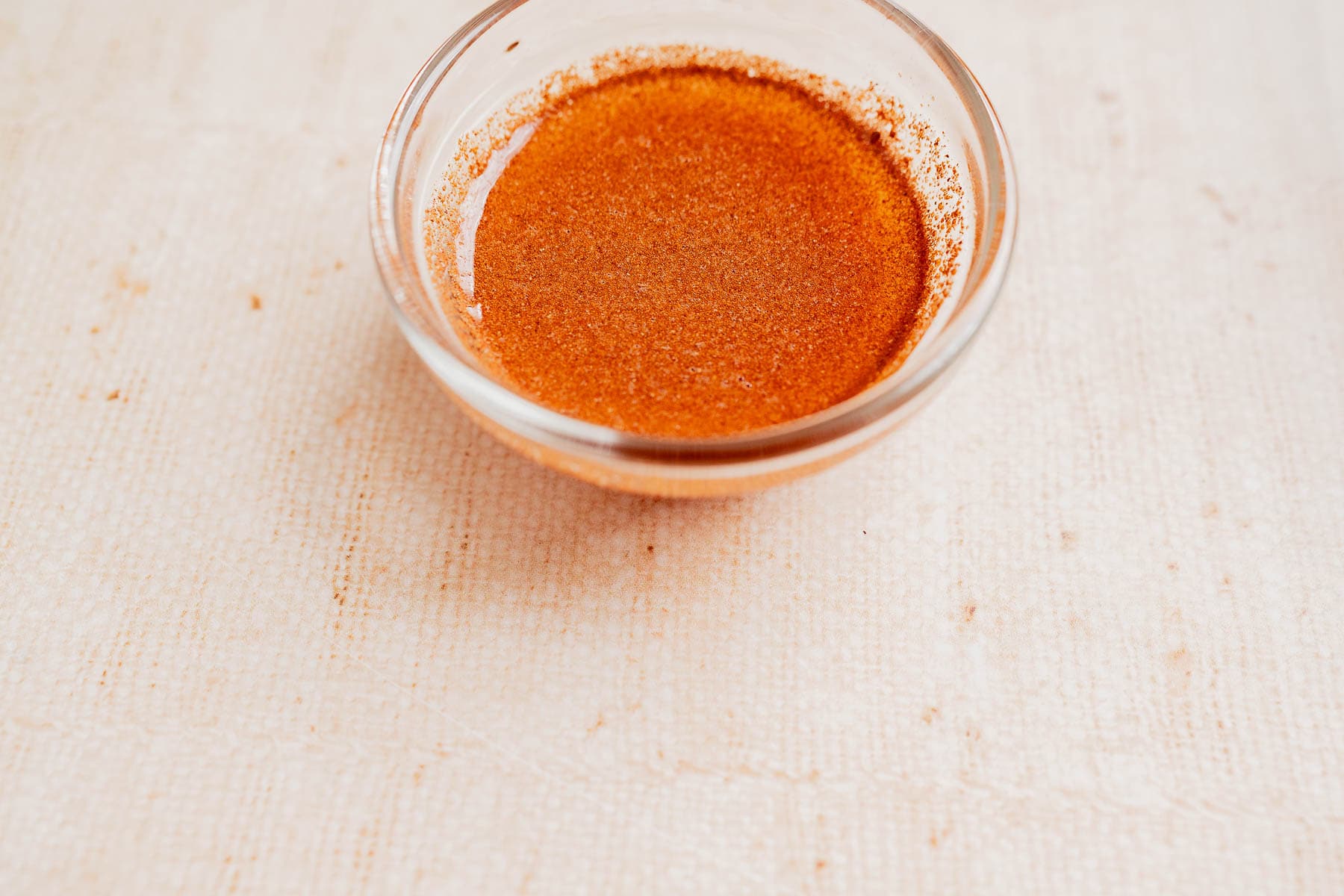 A small glass bowl filled with a reddish-brown liquid seasoning, perfect for drizzling over christmas fruit salad, placed on a light textured surface.