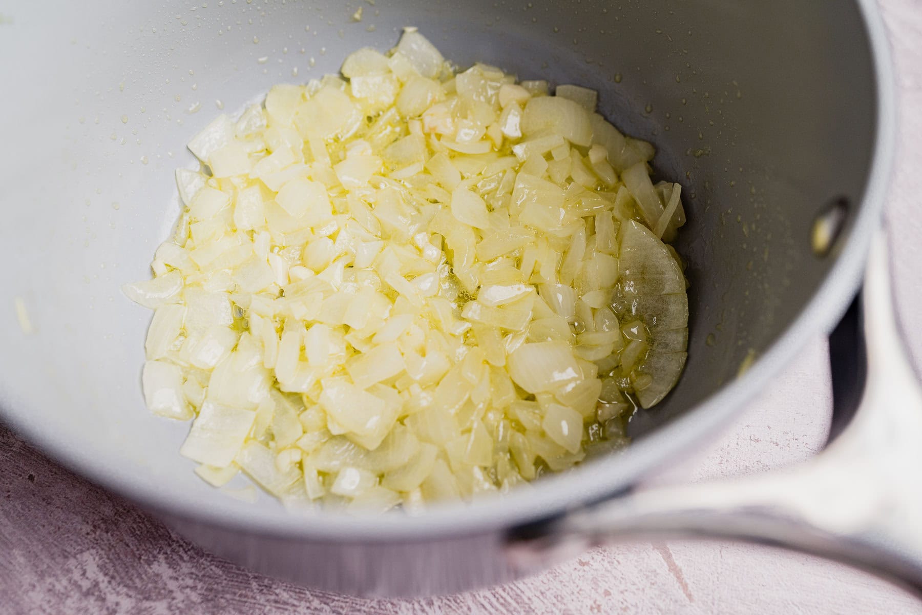 Chopped onions sautéing in oil in a silver saucepan, ready to add rich flavor to a comforting potato casserole.