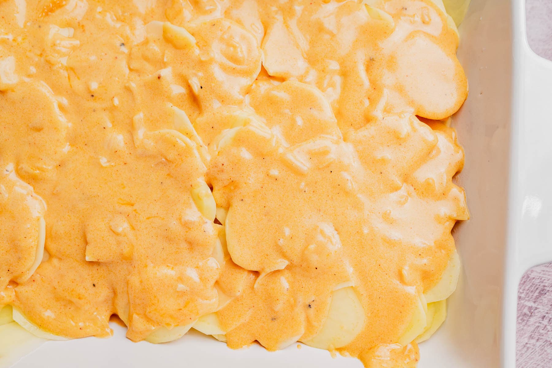 Sliced potatoes arranged in a white baking dish, covered with a creamy orange sauce, make this classic potato casserole irresistible.