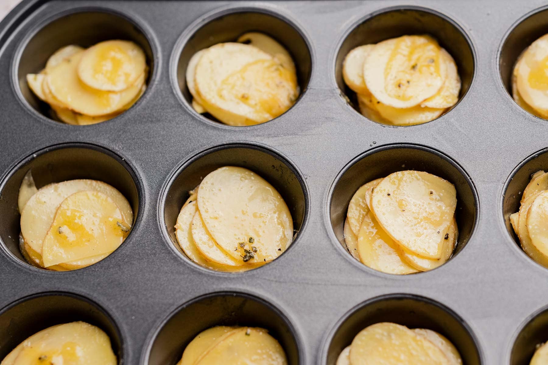 Muffin tin potatoes are thinly sliced raw potatoes, perfectly seasoned and arranged in a muffin tin, ready to be baked into crispy, golden stacks.