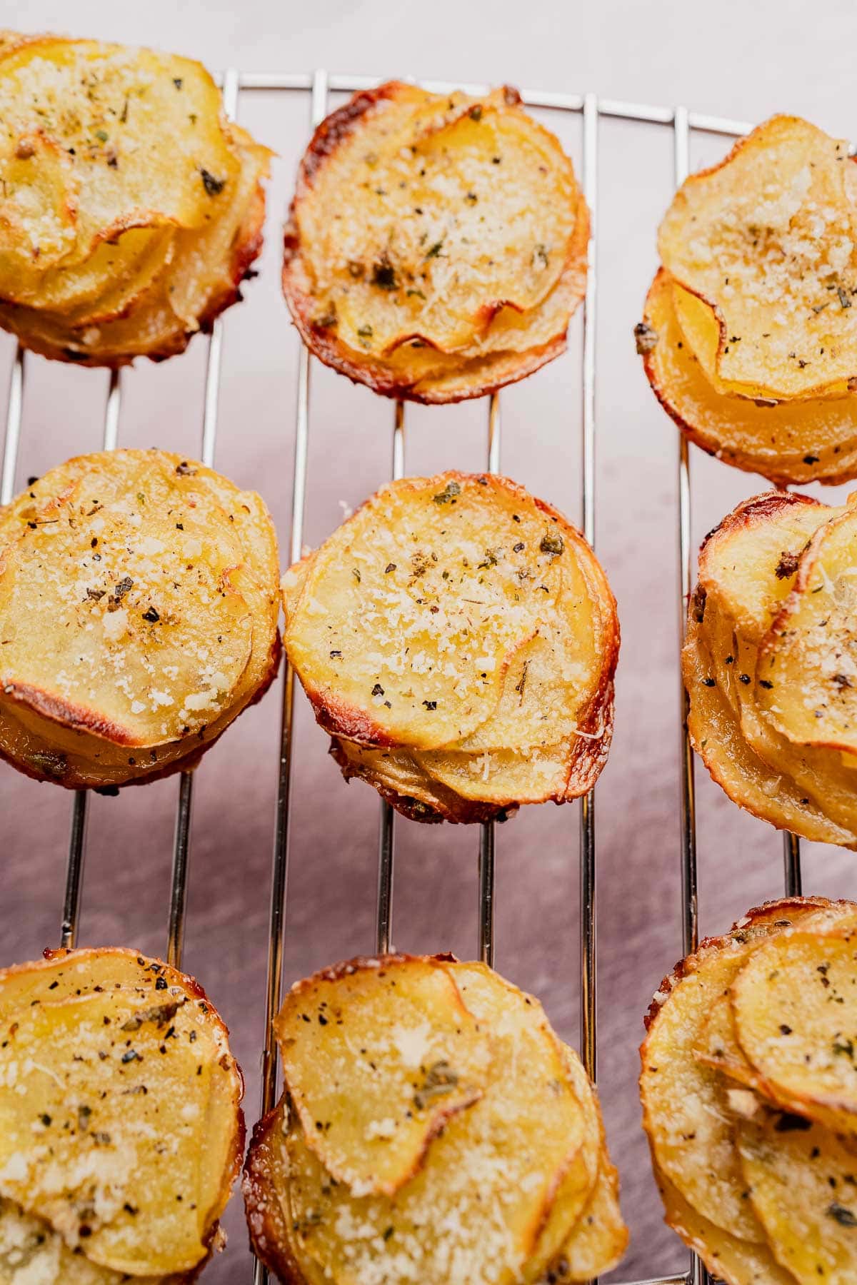 Slices of roasted muffin tin potatoes stacked in muffin shapes, topped with herbs and grated cheese, cooling on a metal rack.
