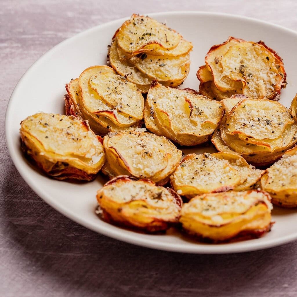 A white plate filled with stacked, thinly sliced muffin tin potatoes, roasted to perfection and seasoned with herbs and black pepper.