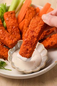 A hand holding a fried food stick with dipping sauce.
