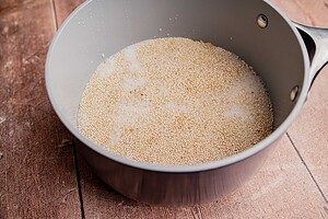 A saucepan filled with uncooked quinoa soaking in water, ready to be transformed into a wholesome quinoa breakfast porridge, sits on a wooden surface.