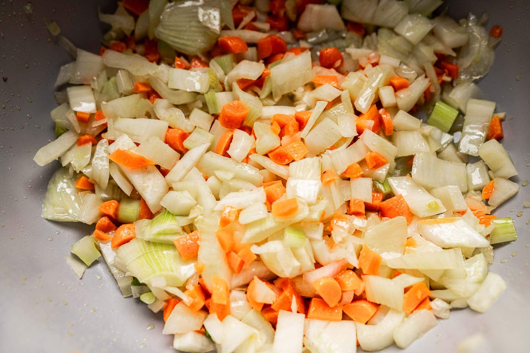 Chopped onions, carrots, and celery in a bowl, ready to add flavor and depth to a hearty Tuscan white bean soup.