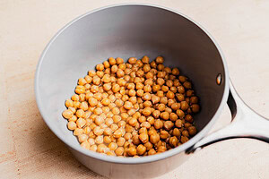 A saucepan containing cooked chickpeas with some liquid at the bottom, placed on a light-colored surface, perfect for making musabaha.
