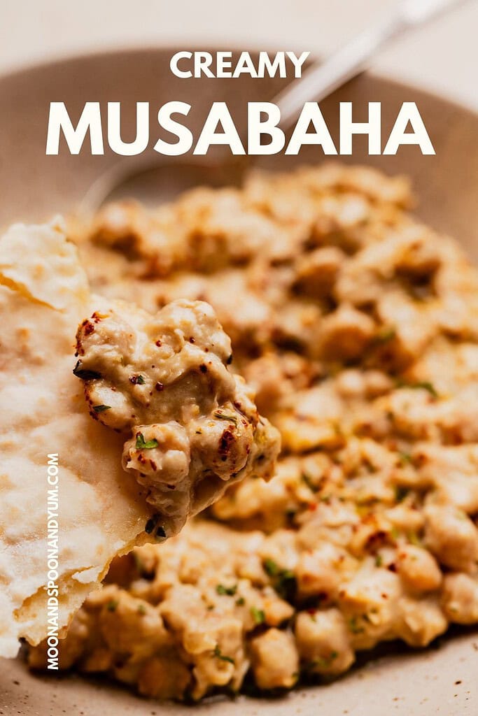 A close-up of creamy musabaha, a traditional chickpea dish, served on a plate, with a piece of bread scooping up the rich blend.