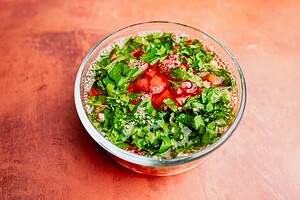 A glass bowl filled with chopped tomatoes, onions, cilantro, aji picante, and juices, set on an orange surface.
