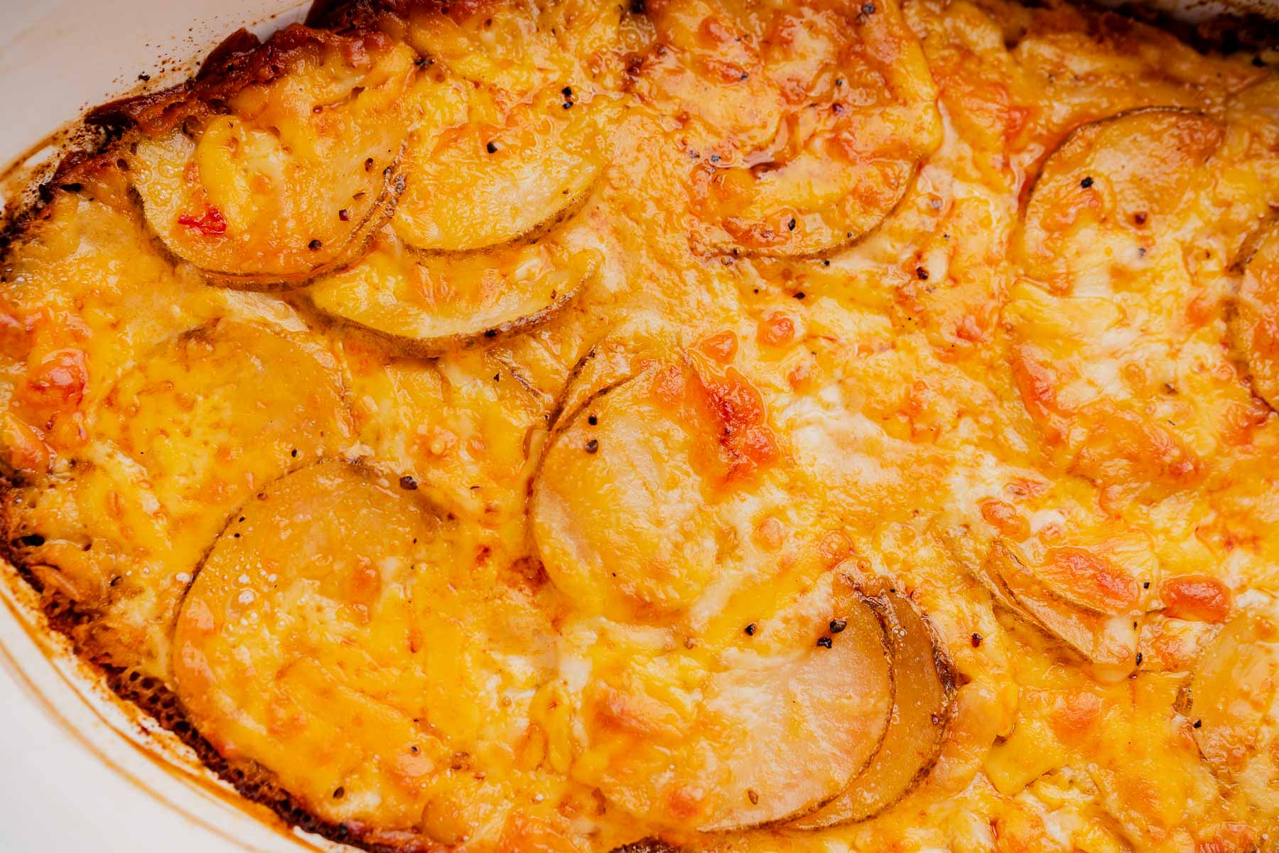 Close-up of a baked buffalo potato casserole with browned edges and visible potato slices covered in melted, spicy cheese.