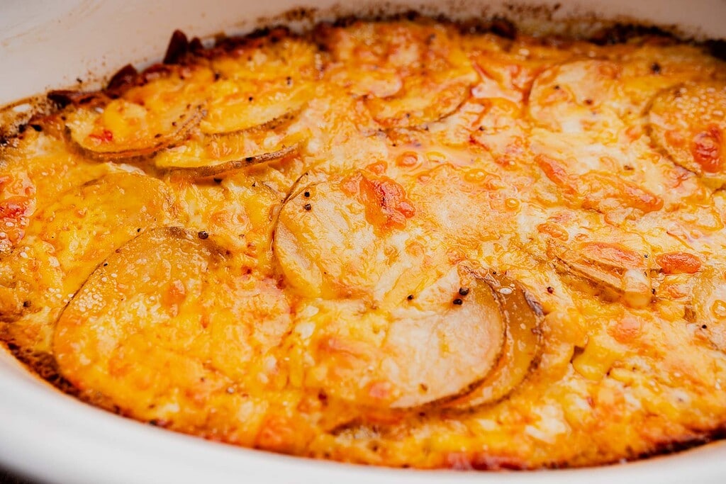Close-up of a baked buffalo potato casserole with golden, bubbly cheese on top and visible potato slices.