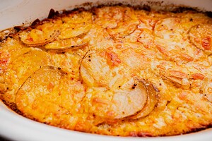 Close-up of a baked buffalo potato casserole with golden, bubbly cheese on top and visible potato slices.