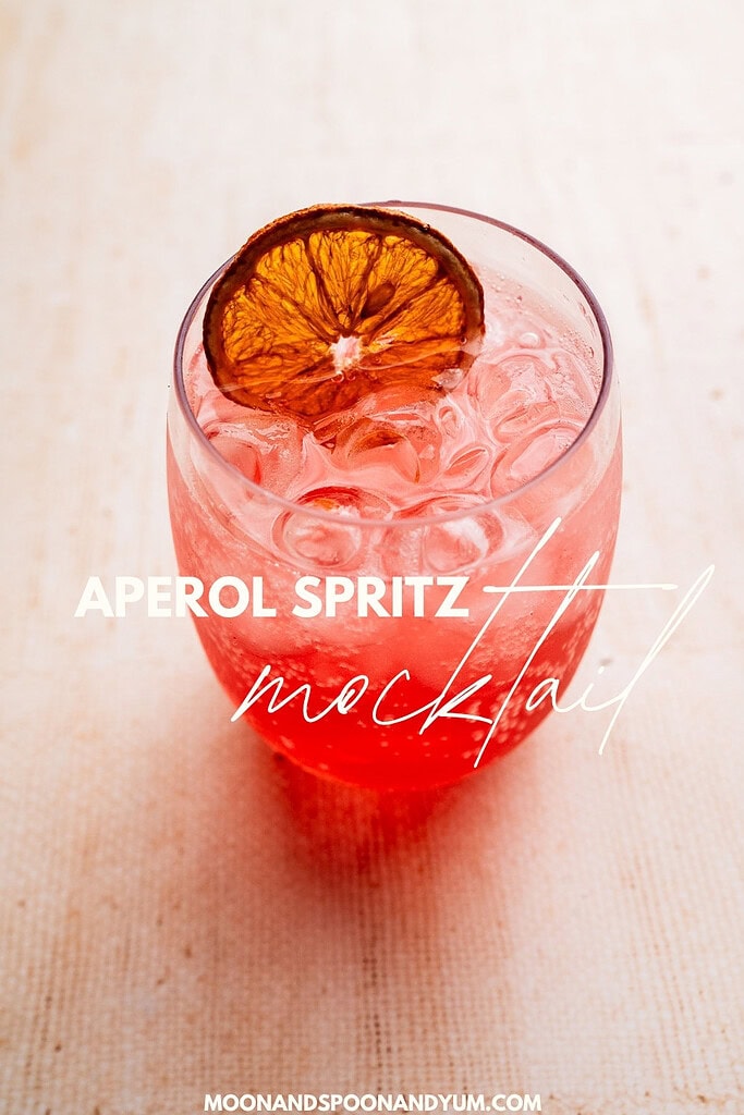 A glass of refreshing Aperol spritz mocktail with ice and a dried citrus slice garnish, elegantly placed on a light surface.
