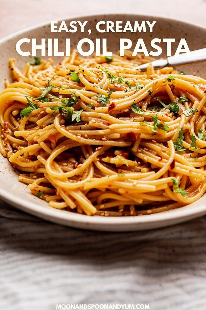 A plate of chili oil pasta coated in a creamy sauce, garnished with chopped parsley, with a fork on the side. Text on image reads “Easy, Creamy Chili Oil Pasta.”.