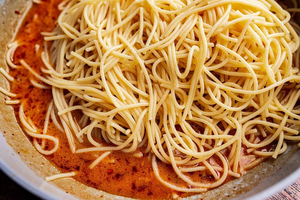 Cooked spaghetti noodles in a bowl, tossed with a vibrant red, oily chili oil pasta sauce.