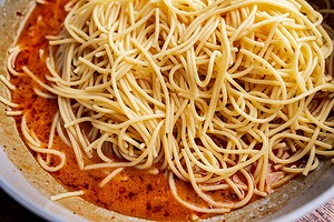 Cooked spaghetti noodles in a bowl, tossed with a vibrant red, oily chili oil pasta sauce.