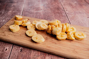 Air fryer sweet plantains, perfectly sliced, are arranged on a wooden cutting board, placed on a rustic wooden surface.