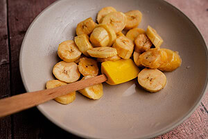 Sliced bananas in a beige bowl with a yellow spatula on a wooden surface, perfect for making air fryer sweet plantains.