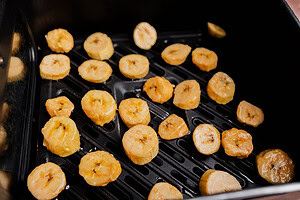 Sliced air fryer sweet plantains are spread out inside the basket, ready for cooking.