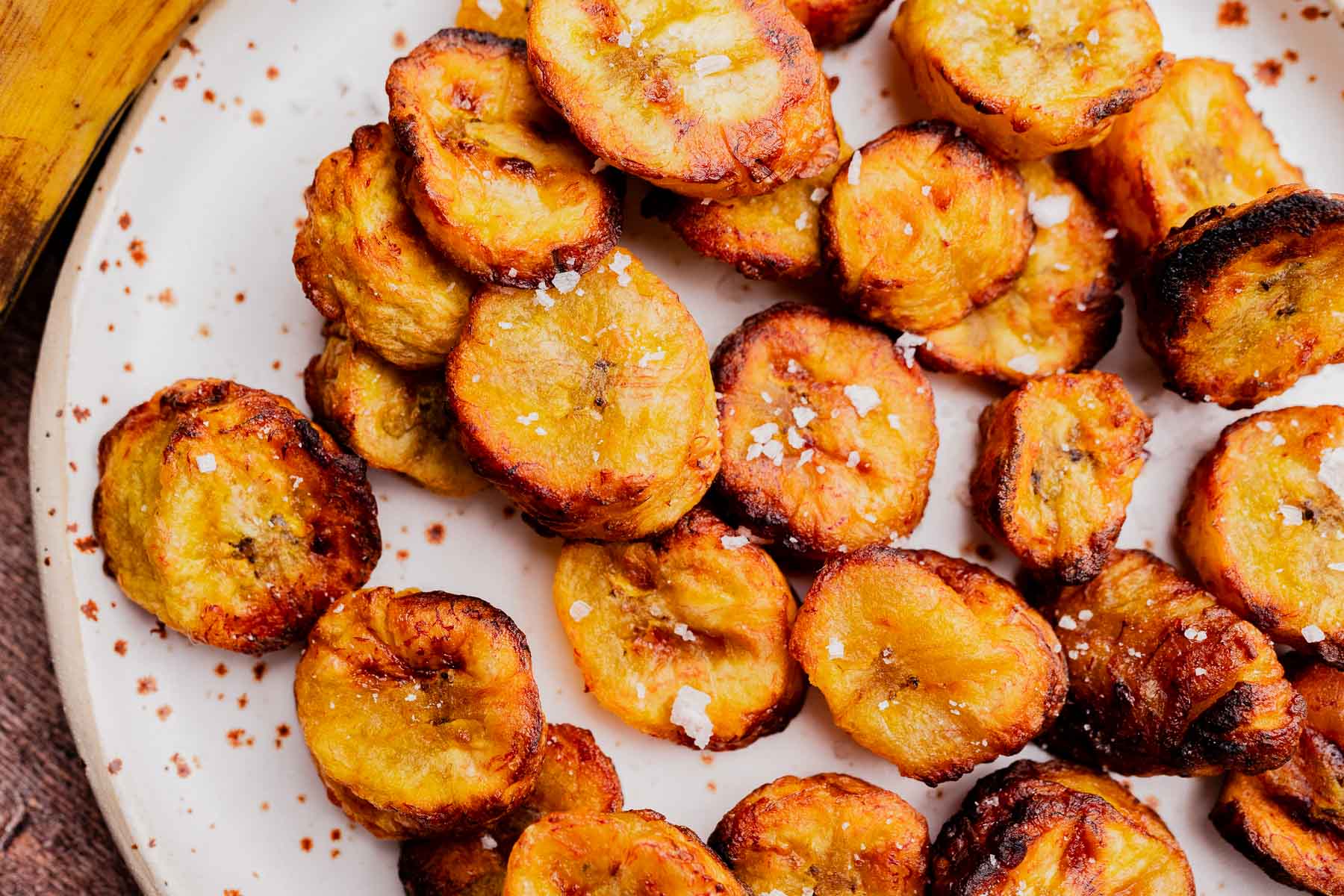 A plate of golden-brown air fryer sweet plantains slices topped with coarse salt, arranged closely on a white surface.