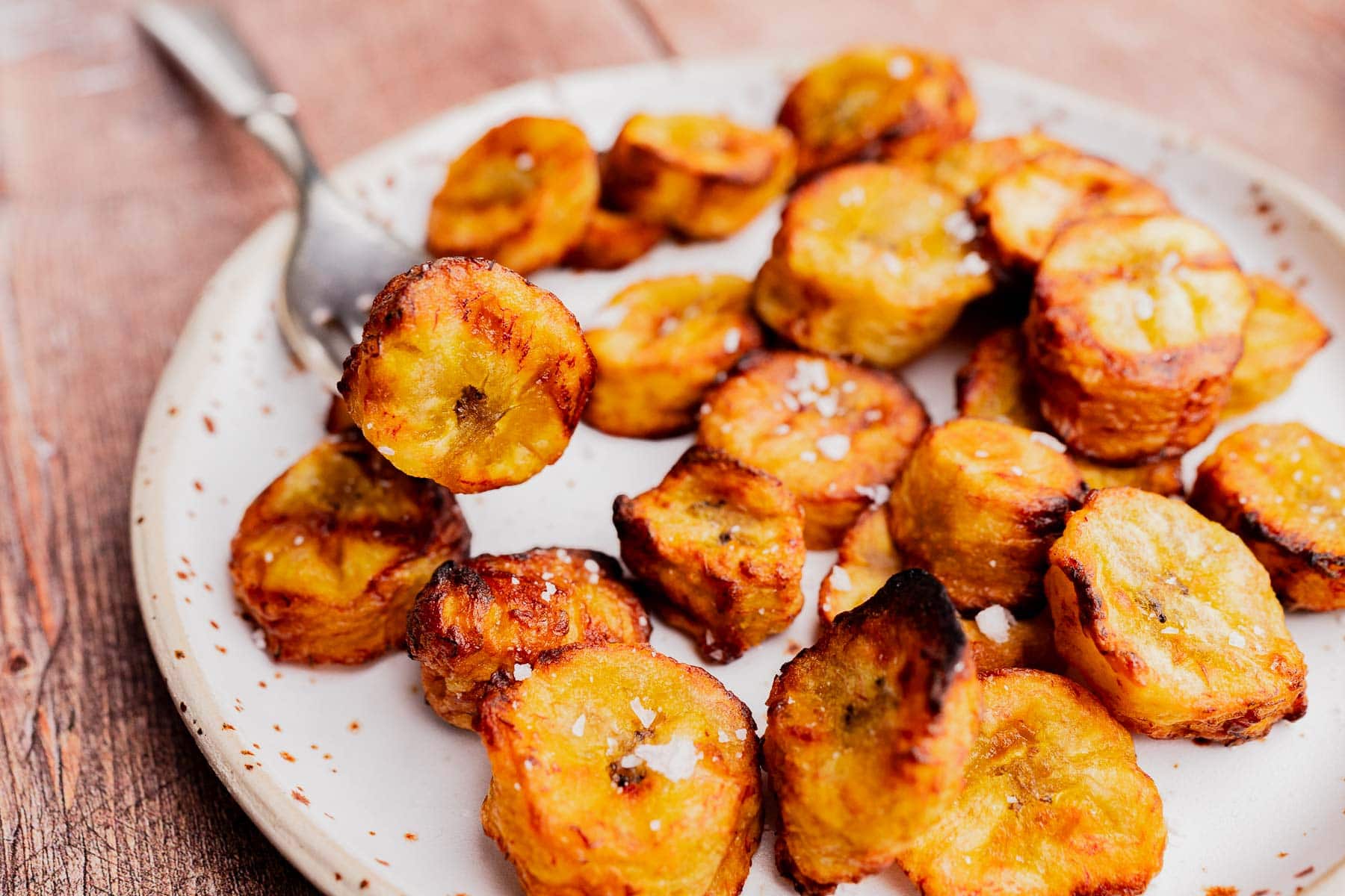A plate of air fryer sweet plantains, sliced and sprinkled with salt, served on a speckled plate with a fork.