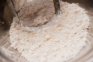 A pastry cutter blends flour and fat in a metal bowl, creating a coarse, crumbly mixture—ideal for making gluten free scones.