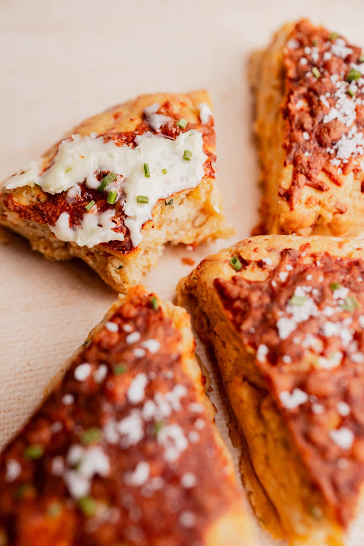 Four triangular pieces of savory gluten free scones, topped with herbs and salt; one piece has a bite taken out and is spread with butter and chives.