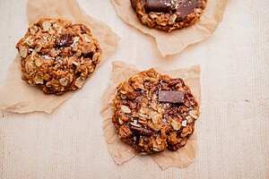 Three gluten free oatmeal chocolate chip cookies rest on brown parchment paper against a neutral background.