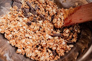 A close-up of gluten free oatmeal chocolate chip cookie mixture being stirred with a wooden spatula in a metal bowl.