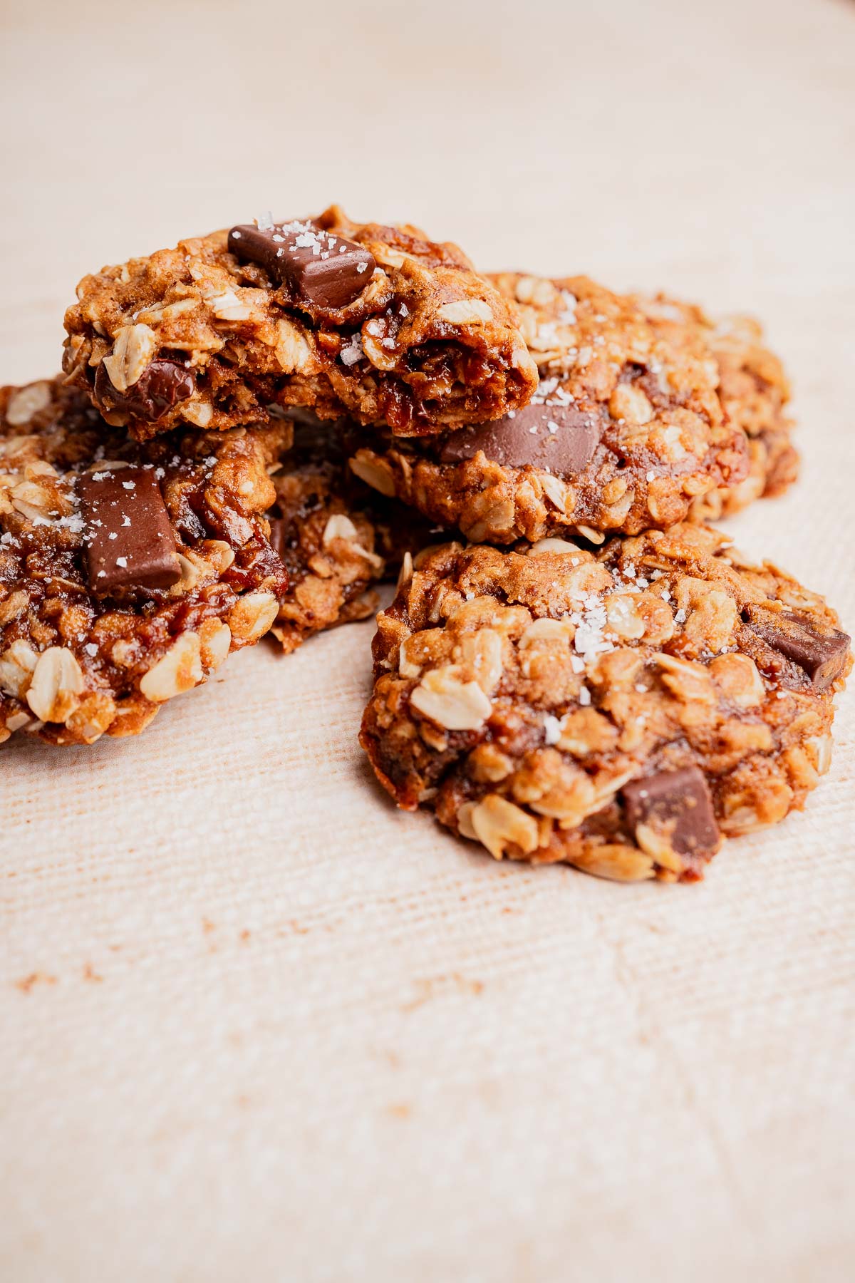Three gluten free oatmeal chocolate chip cookies with visible oats and chocolate chunks are stacked on a light-colored surface.