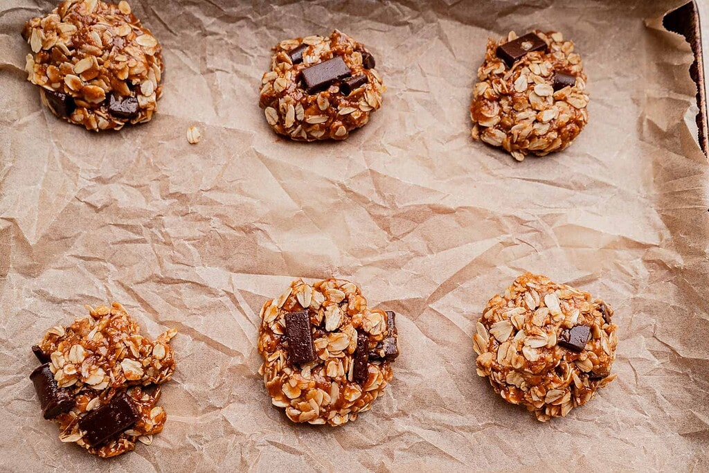 Six unbaked gluten free oatmeal chocolate chip cookies arranged on a sheet of crumpled parchment paper.