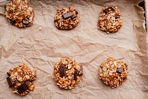 Six unbaked gluten free oatmeal chocolate chip cookies arranged on a sheet of crumpled parchment paper.