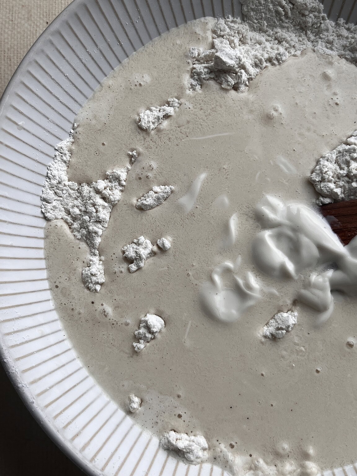 A close-up of a bowl containing flour and a liquid mixture being stirred with a wooden spoon—perfect for making gluten free butter swim biscuits.