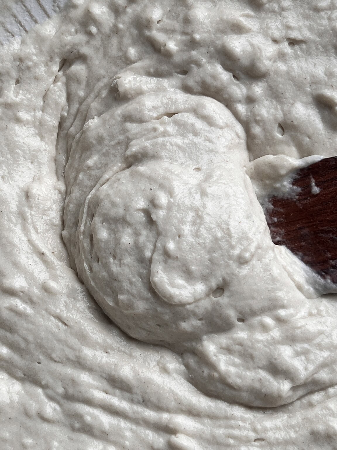 Close-up of a thick, creamy batter for gluten free butter swim biscuits being mixed with a wooden spoon.