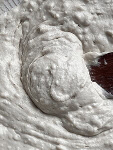 Close-up of a thick, creamy batter for gluten free butter swim biscuits being mixed with a wooden spoon.
