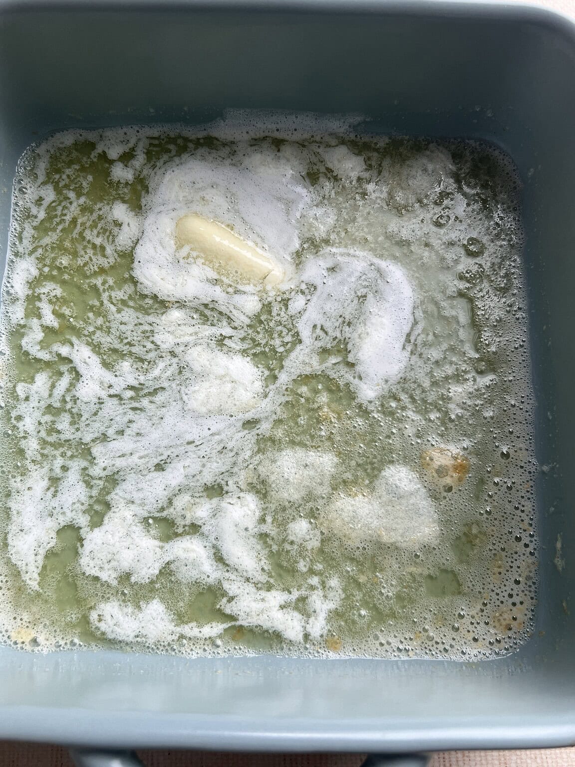 Melted butter with white foam on the surface in a blue rectangular dish, perfect for making gluten free butter swim biscuits.