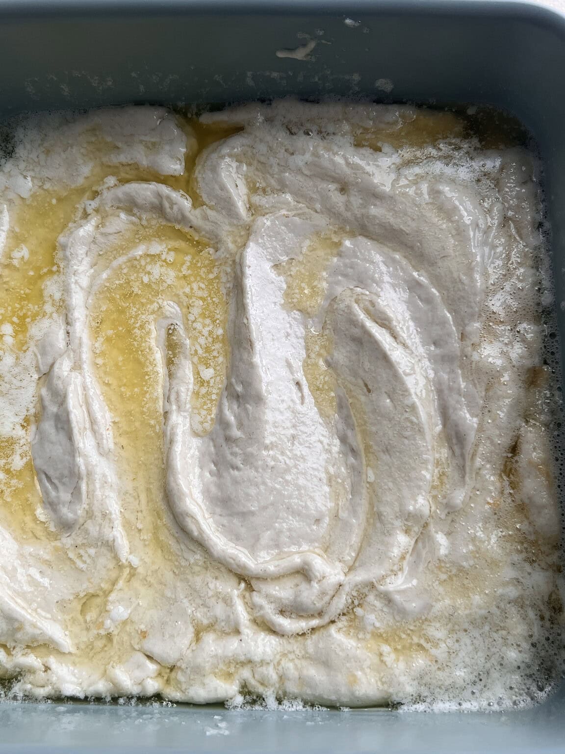 Unbaked cake batter swirled with melted butter in a blue baking dish, reminiscent of gluten free butter swim biscuits.