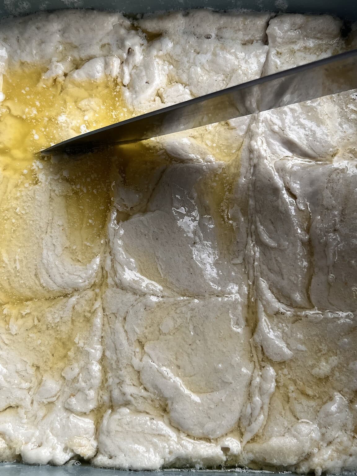 A baking dish filled with unbaked gluten free butter swim biscuits, divided into squares with a knife and topped with melted butter.