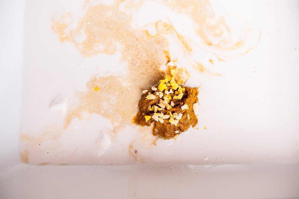 Close-up of a brownish clump resembling baked dumplings and small yellowish-white particles floating in cloudy, off-white liquid inside a container.