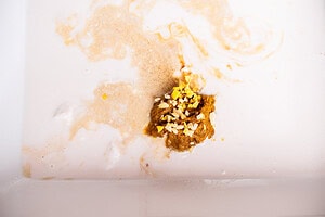 Close-up of a brownish clump resembling baked dumplings and small yellowish-white particles floating in cloudy, off-white liquid inside a container.