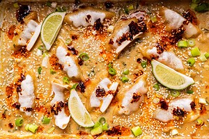 Baked dumplings in a creamy sauce topped with chili oil, sesame seeds, chopped green onions, and lime wedges.