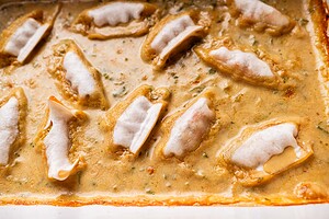 Several baked dumplings are arranged in a creamy, light brown sauce inside a baking dish.