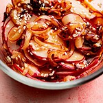 Close-up of a spicy radish recipe featuring thinly sliced radishes mixed with sesame seeds and a dark sauce in a glass bowl.