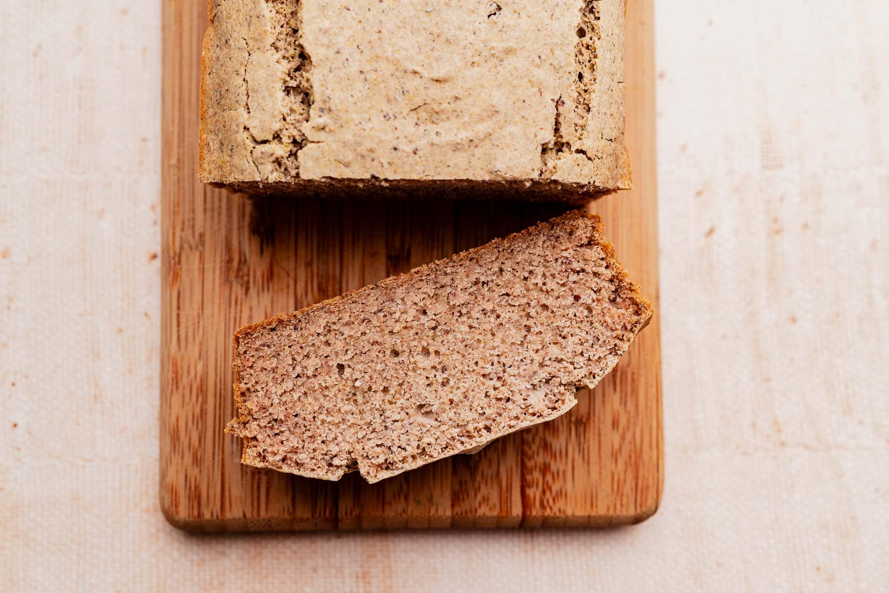 A loaf of buckwheat bread with one thick slice cut, placed on a wooden cutting board.