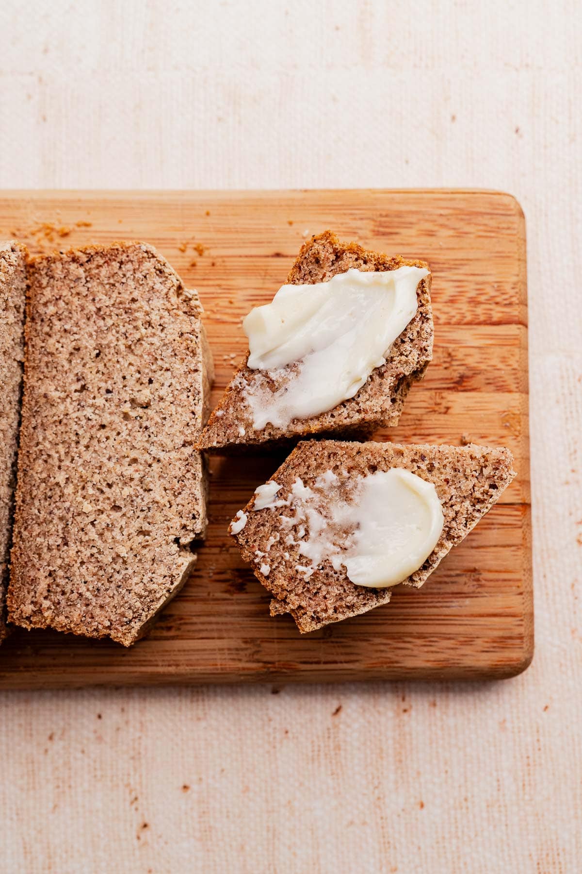 Slices of buckwheat bread on a wooden cutting board, with two pieces topped with a spread of butter.