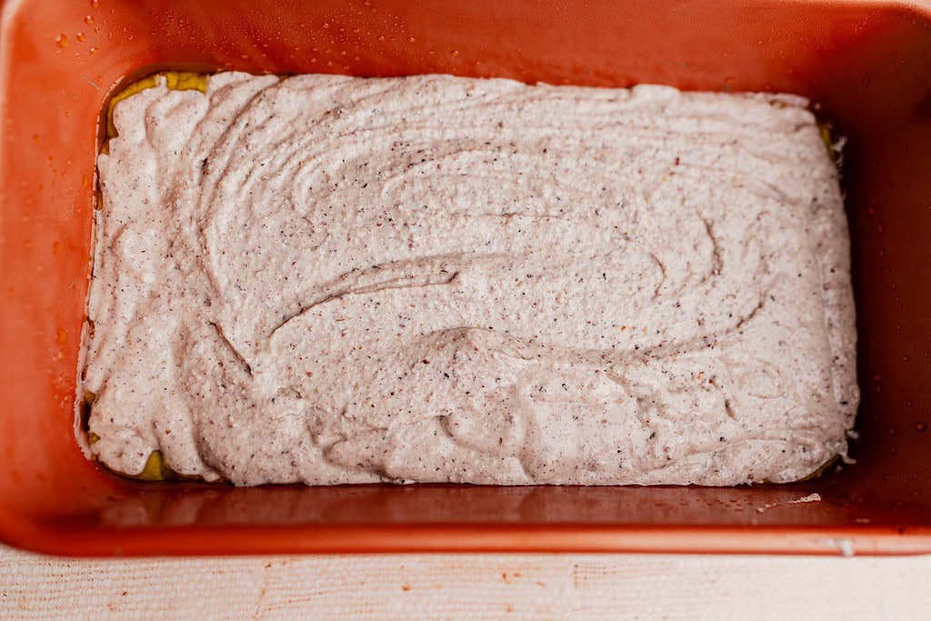 A rectangular baking dish filled with an even layer of raw buckwheat bread batter, ready to be baked.