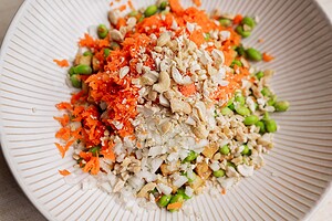 A close-up of a bowl featuring chopped carrots, onions, tofu, edamame, and crushed cashews arranged in separate piles—perfect for a vibrant tofu edamame salad.